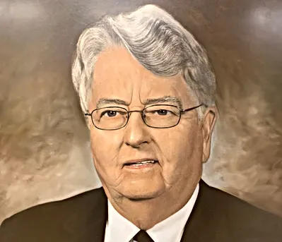 Displayed is a picture of Dr. Rose in his suit. He is wearing glasses.